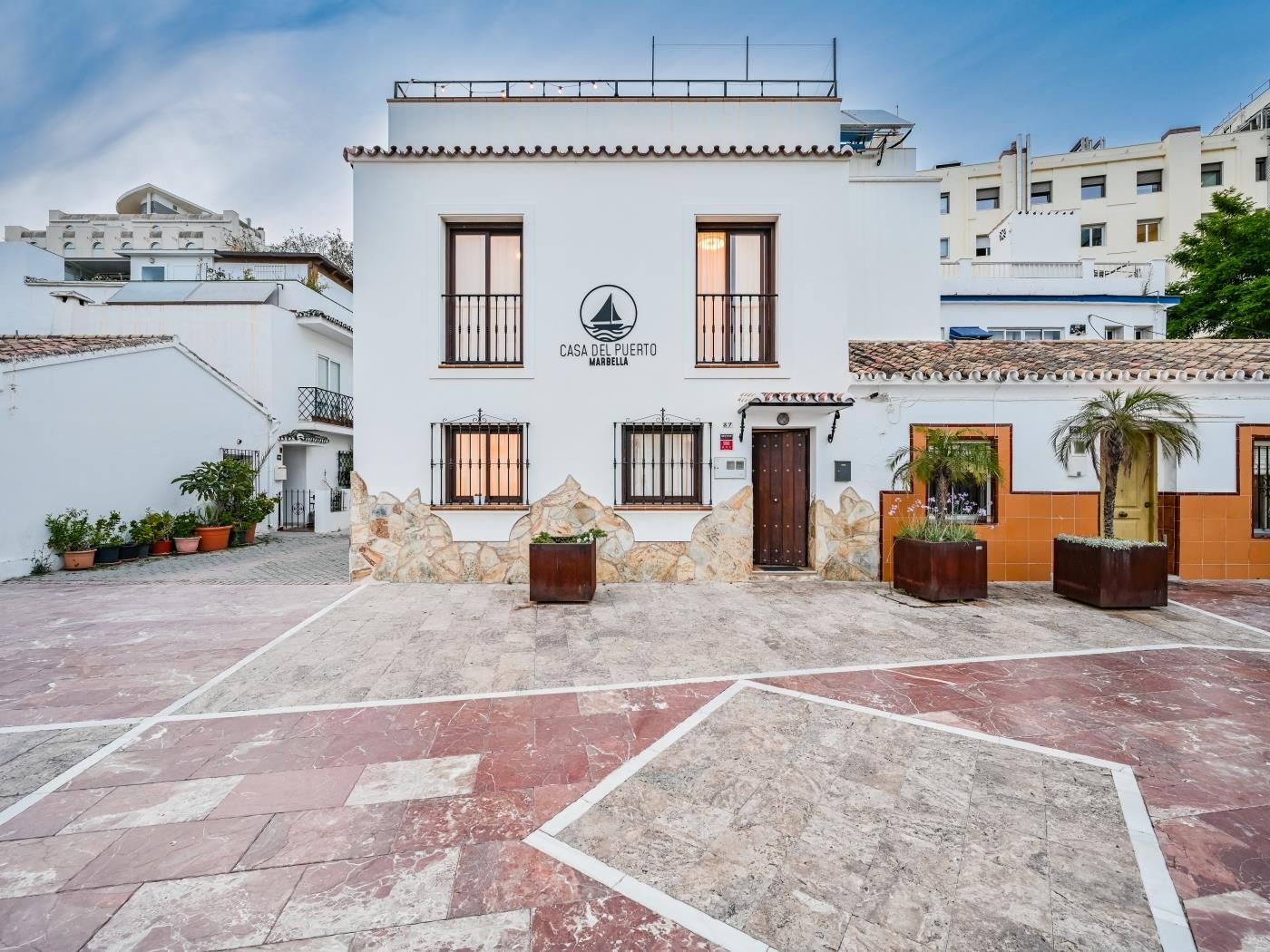 Front façade of Casa del Puerto from the plaza at dusk, in Marbella's marina quarter